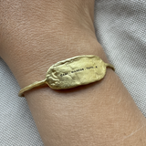 Gold bracelet with engraved text on a wrist against a neutral background