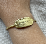 Gold bracelet with engraved text on a wrist against a neutral background